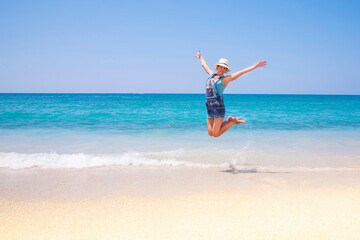 Happy young woman jumping on the beach.Beautiful free young girl jumps on the exotic sea, happy brunette girl in dress running on tropical beach with white sand. Enjoyment. Lifestyle. Freedom. 