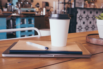 Laptop, notebook, pen and a hot drink (tea or coffee) on a table in a cafe. Distance learning or work concept