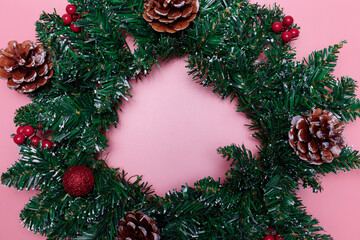 Fototapeta na wymiar Christmas wreath with red balls, berries and pine cones on a pink background. Copy space.