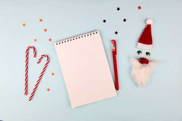 Christmas composition, wish list concept. Notebook with pen, Santa Claus with red hat and beard on light blue background. Flat lay, top view.