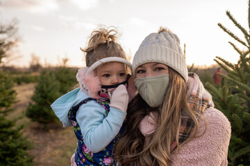 Young mom and toddler girl wearing cloth face masks at the tree farm