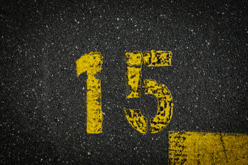Grey asphalt road, yellow painted number fifteen on grey street, yellow lines like a corner on the...