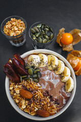 Top view chocolate smoothie bowls with fruits, nuts, seeds and homemade granola, banana for healthy vegan vegetarian.