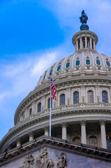 View of American flag on top of entrance to United States Capitol building with marble dome in background with blue sky