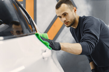 Man in a garage. Worker polish a car. Man in a black uniform.