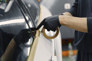 Auto body repair series. Masking car before repaint. Man in a black uniform.