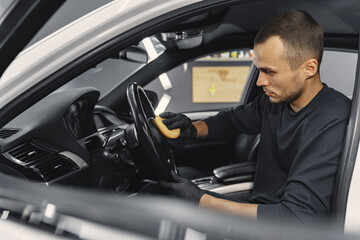 Fototapeta na wymiar Man in a garage. Worker polish inside a car. Man in a black uniform.