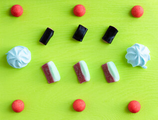 Sweet pattern flat lay for candy shop, colorful italian sweets: marmalade, marshmallow and licorice on green background.