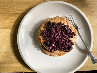 Closeup of a stack of pancakes with a fresh blueberry compote topping on a white plate. From above perspective. Fork on right side.