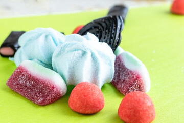 Colorful italian sweets for party: black licorice candies scattered messy on a green background soft focus photo.