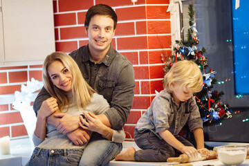Lovely parents with preschool son at the kitchen, baking biscuits, get ready for Christmas celebration, loving father hug beautiful mother, family spend winter holidays concept