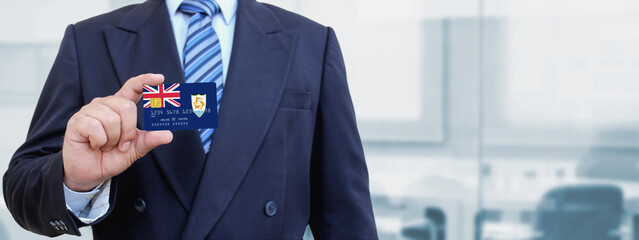 Cropped image of businessman holding plastic credit card with printed flag of Anguilla. Background blurred.
