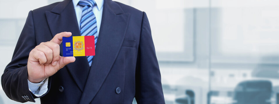 Cropped image of businessman holding plastic credit card with printed flag of Andorra. Background blurred.