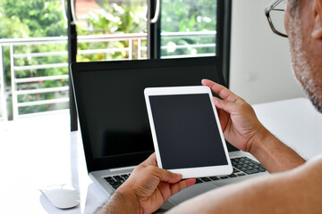 Close Up, People using the tablet device at home. A man holds a white tablet to use the internet in the living room at home during the day, blank black screen for design Copy space, Blurred background
