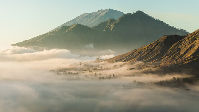 Sunrise view of mount Batur, Abang and Agung volcano in Bali from Pinggan village. Beautiful sunrise and low clouds. Layered minimalist landscape.