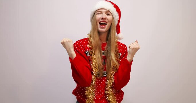 rejoicing young woman wearing christmas sweater and santa claus hat, having fun and dancing on white background, celebrating new year