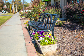 A park bench next to a side walk with colorful flowers