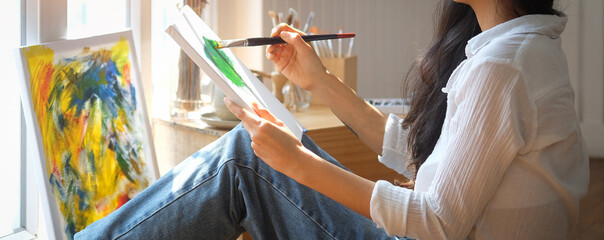 Cropped shot of concentrate female artist painting on cotton canvas with oil paint at home.