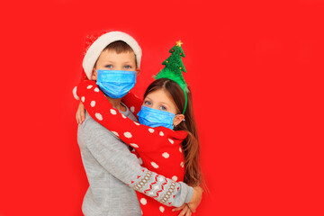 Children in respiratory masks and New Year's outfits hug on a red background during the quarantine period