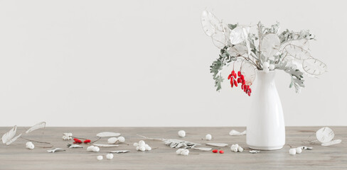bouquet with lunaria and red berries in white vase on wooden table