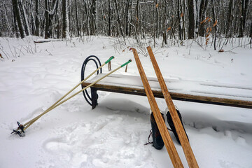 Skis and ski poles on a snow-covered bench in the woods