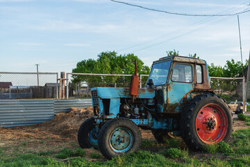 Naklejka premium Abandoned old tractor in the village. Blue tractor with red wheel