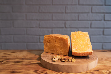 A head of aged cheese cut in half on a wooden Board with various nuts on the background of a brick wall