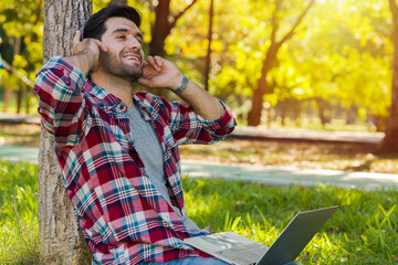 Caucasian man sits comfortably in the park with a laptop.