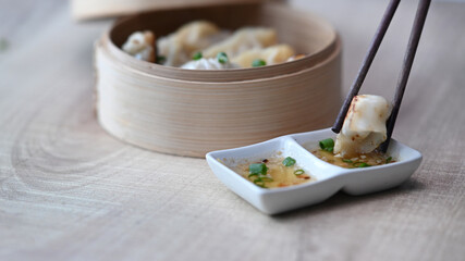 Close up shot of chopsticks holding dumpling dipping into plum sauce on wood table.