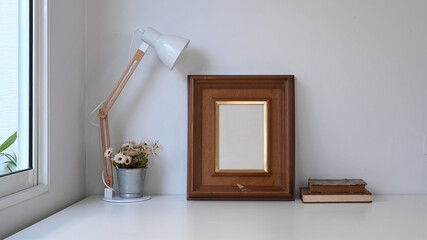 Vintage workspace with empty frame, pot plant, lamp and old book on white table.