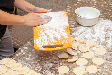 A woman sprinkles flour on a board.