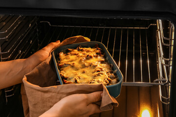 Woman taking baking dish with tasty rice casserole out of oven