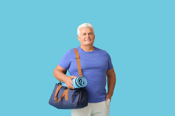 Sporty senior man with bag and yoga mat on color background