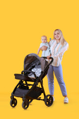 Fototapeta na wymiar Woman with her cute baby and stroller on color background