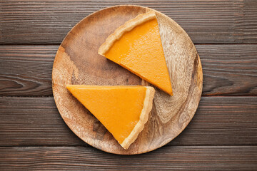 Plate with slices of tasty pumpkin pie on wooden background