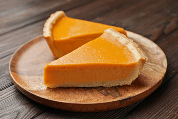 Plate with slices of tasty pumpkin pie on wooden background, closeup