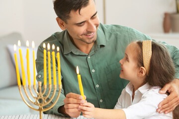 Happy father and daughter lighting candles for celebrating Hannukah at home