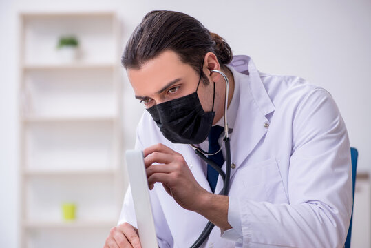 Young male doctor with stethoscope repairing computer