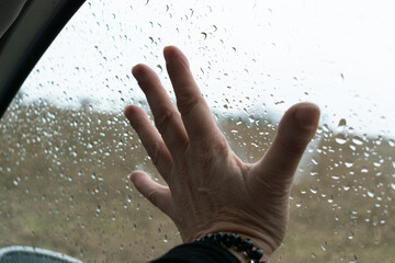 Mano en el cristal con gotas de agua en el cristal, dentro del coche
