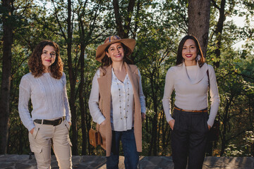 Three beautiful women smiling portrait. Sisters and friends standing posing at the camera in natural background.