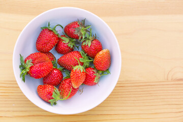 Red strawberries are in a plate. The plate is on a wooden surface.