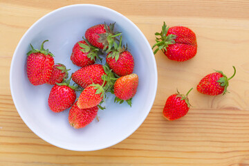 Red strawberries are in a plate. The berries are on a wooden surface.