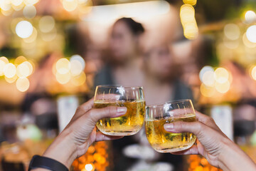 Friends clinking glass of with whisky for celebration against background of bokeh lights.