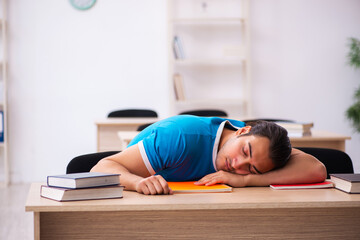 Exhausted male student preparing for the exams in the classroom