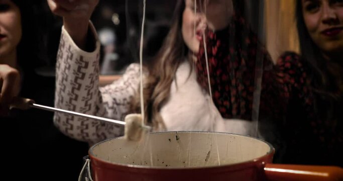 Cheese fondue with three beautiful women eating the cheese bread. We can see the bread soak in the melted cheese. Perfect meal with friends 4K