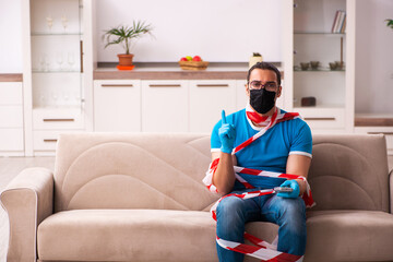 Obraz premium Young man watching tv at home in pandemic concept