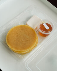 Stack of pancakes in a container transparent clear box with honey and butter isolated on white background.