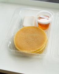 Stack of pancakes in a container transparent clear box with honey and butter isolated on white background.