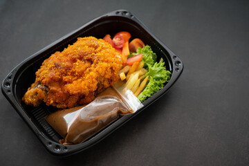 Chicken Chop and fries with  Black Pepper sauce and vegetables. in a take away container.