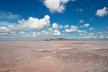 Landscape of a dried up pink salt lake with white clouds in a blue sky
